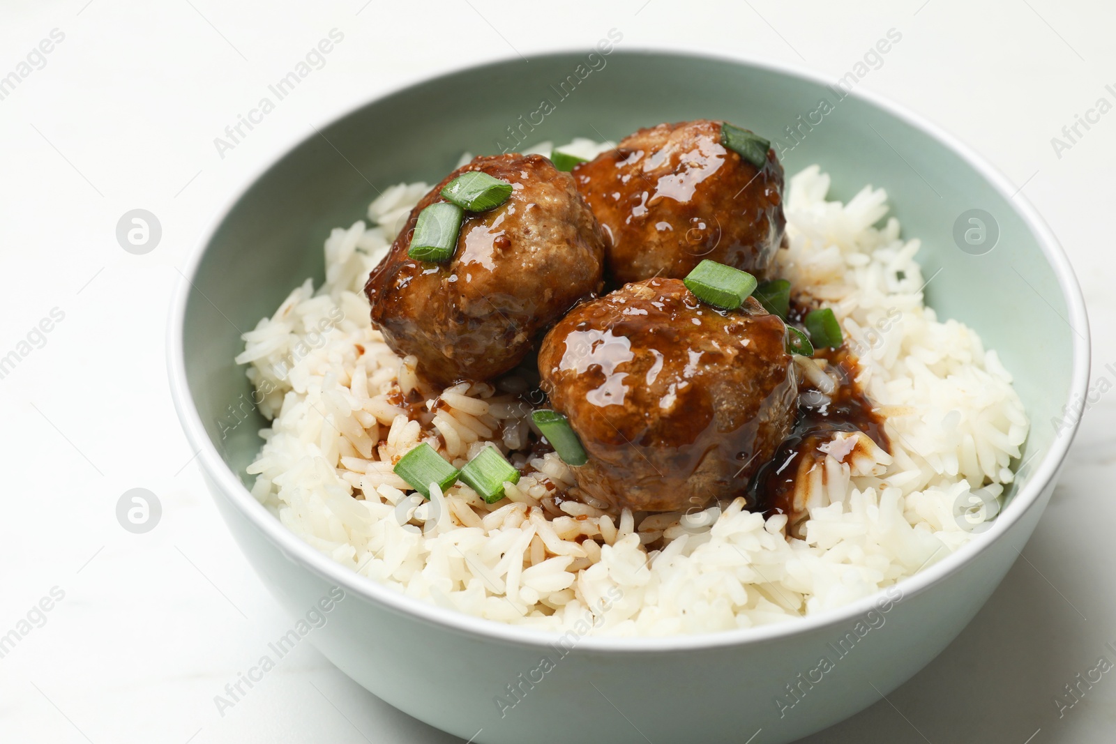 Photo of Delicious rice with meatballs, sauce and green onions in bowl on white table, closeup