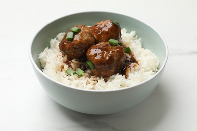 Photo of Delicious rice with meatballs, sauce and green onions in bowl on white marble table, closeup