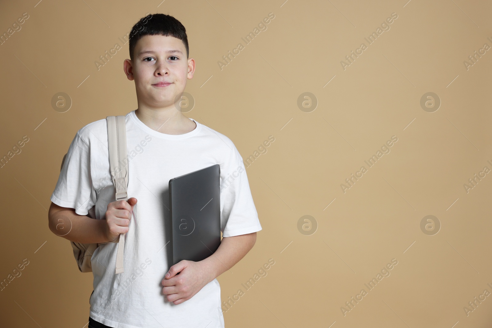 Photo of Portrait of teenage boy with laptop and backpack on beige background, space for text