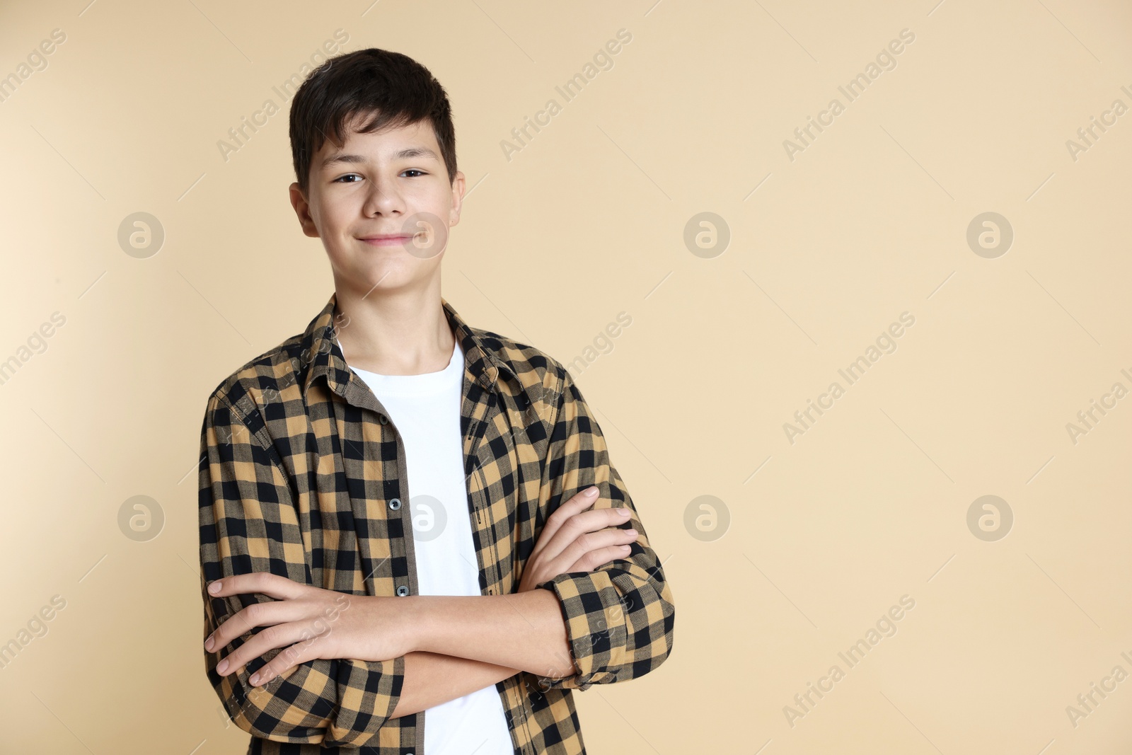 Photo of Portrait of teenage boy with crossed arms on beige background, space for text