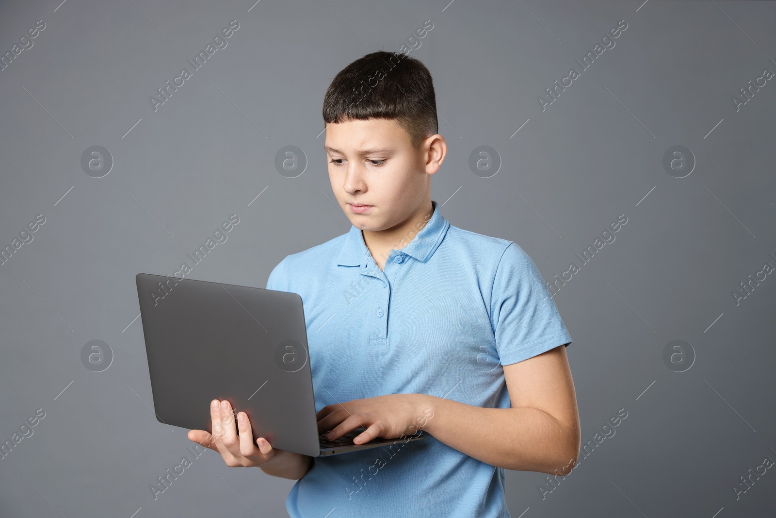 Photo of Portrait of teenage boy with laptop on grey background