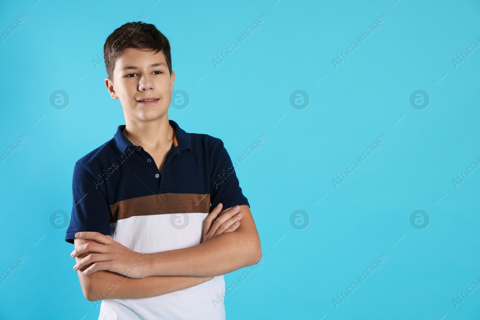 Photo of Portrait of teenage boy with crossed arms on light blue background, space for text