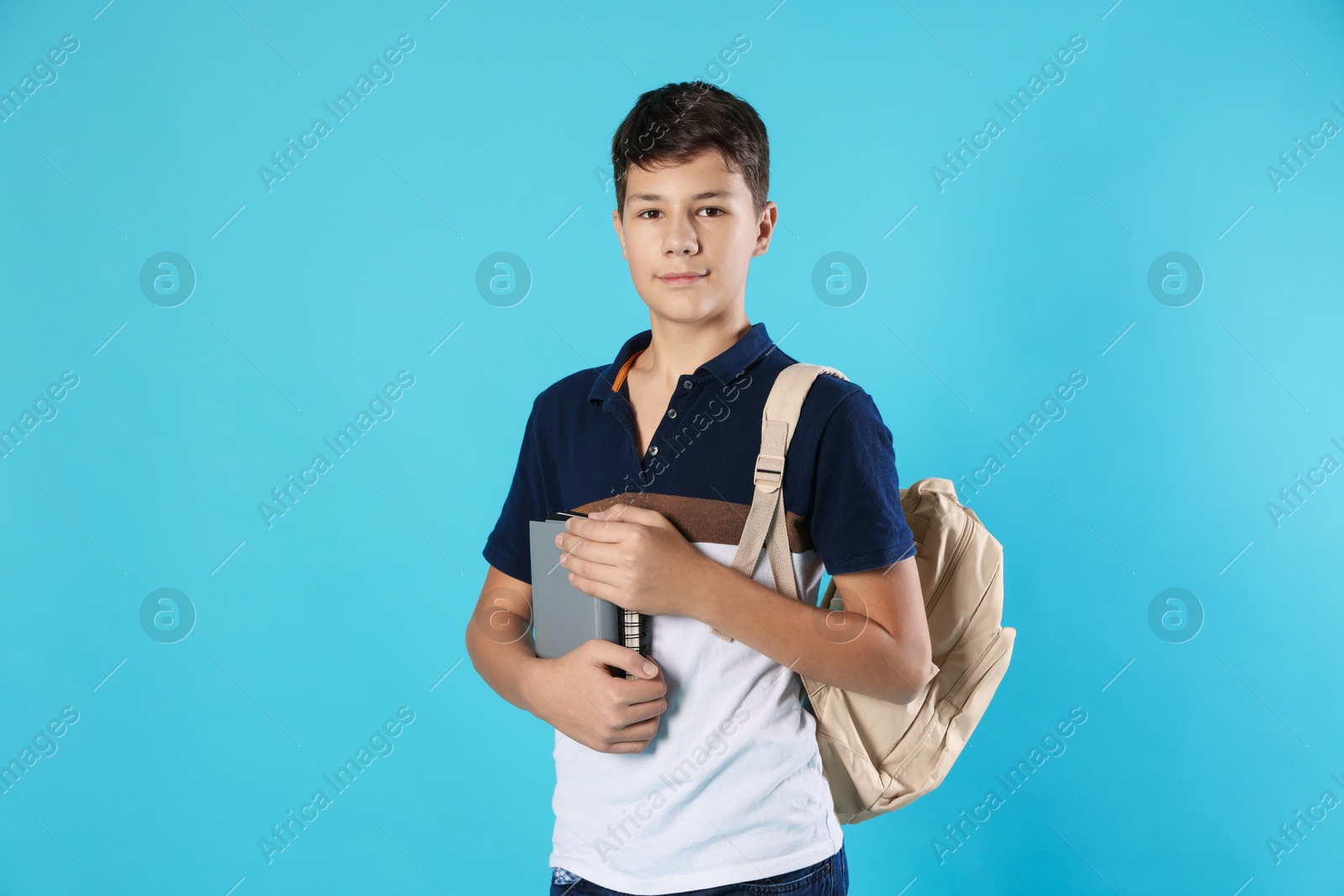 Photo of Portrait of teenage boy with books and backpack on light blue background