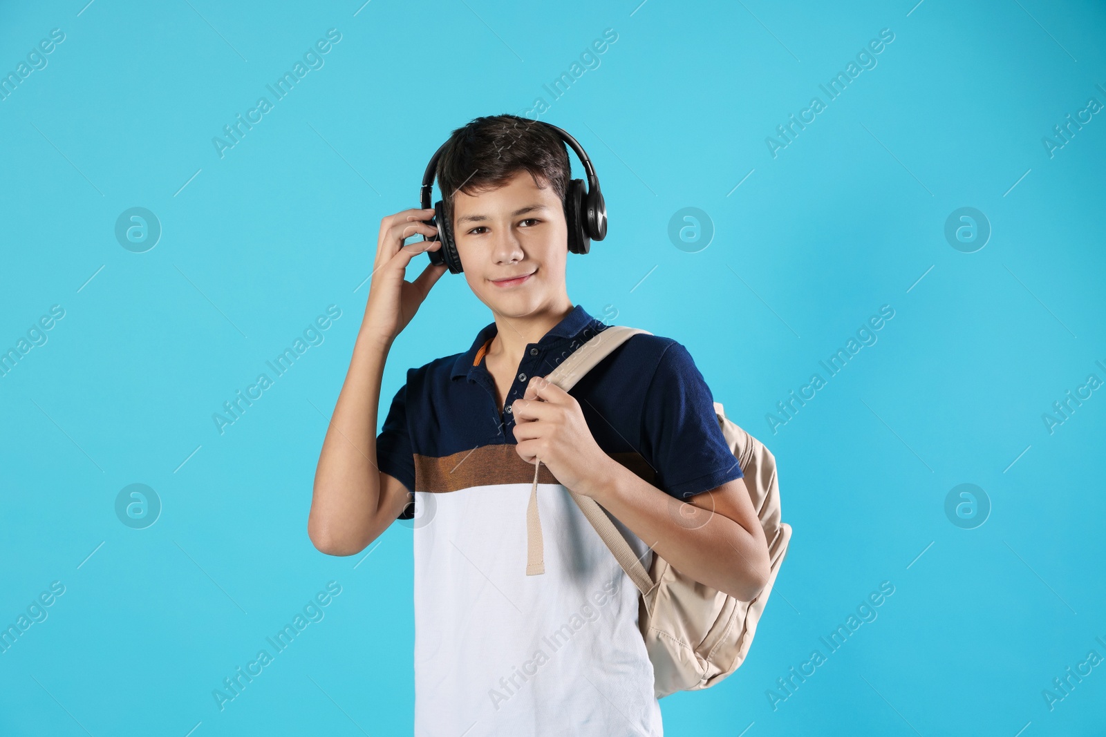 Photo of Portrait of teenage boy with headphones and backpack on light blue background