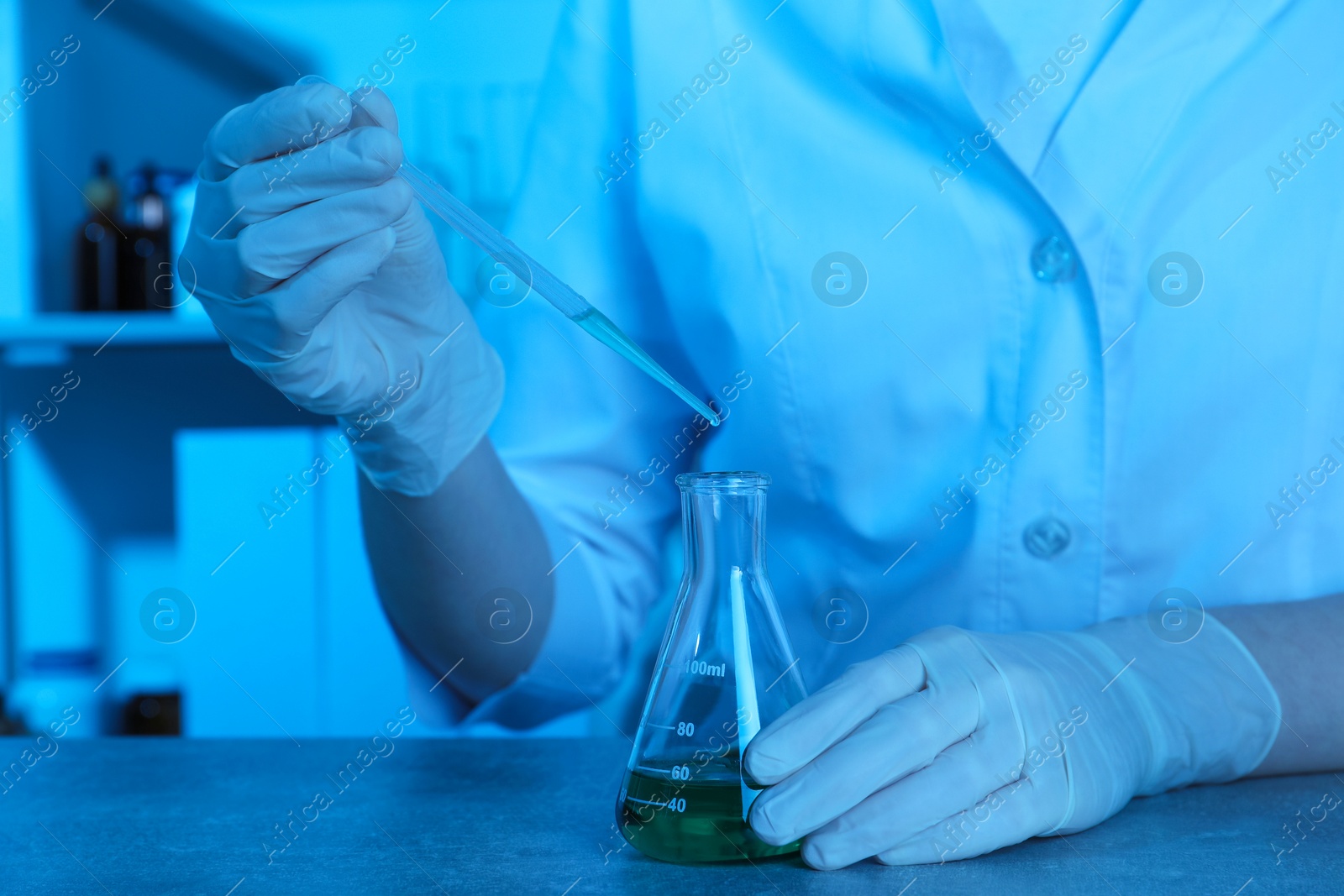 Photo of Laboratory testing. Scientist dripping sample into flask at table indoors, closeup