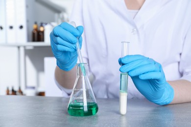 Photo of Laboratory testing. Scientist with test tube taking sample from flask at grey table indoors, closeup