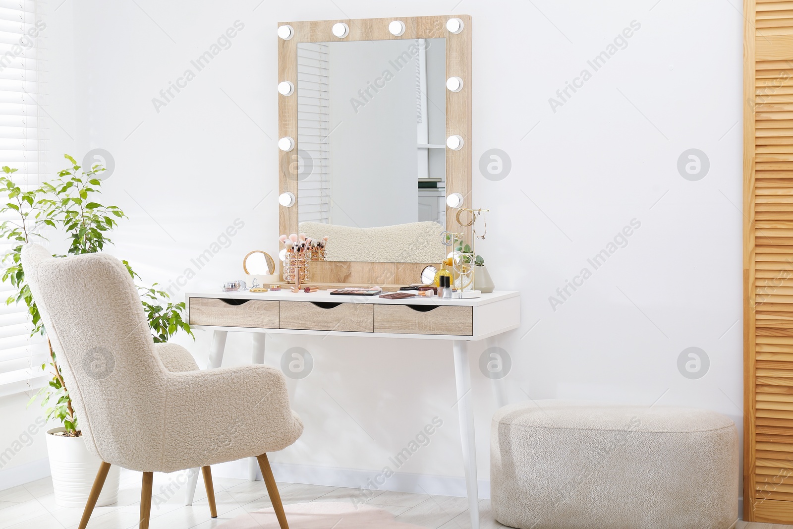 Photo of Makeup room. Dressing table with mirror, different beauty products, jewelry, armchair and houseplant indoors