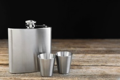 Photo of Hip flask and cups on wooden table, space for text