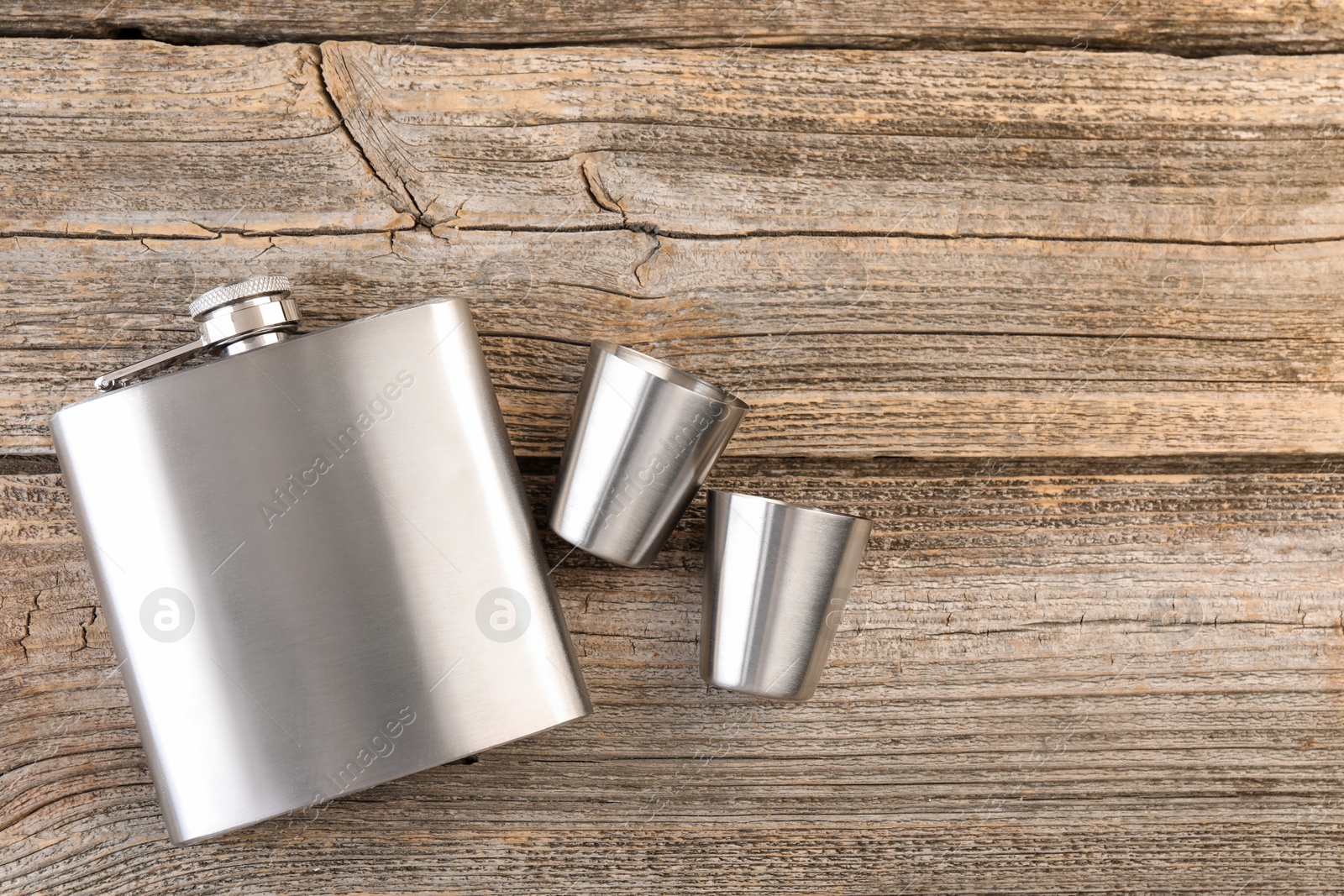 Photo of Hip flask and cups on wooden table, flat lay. Space for text