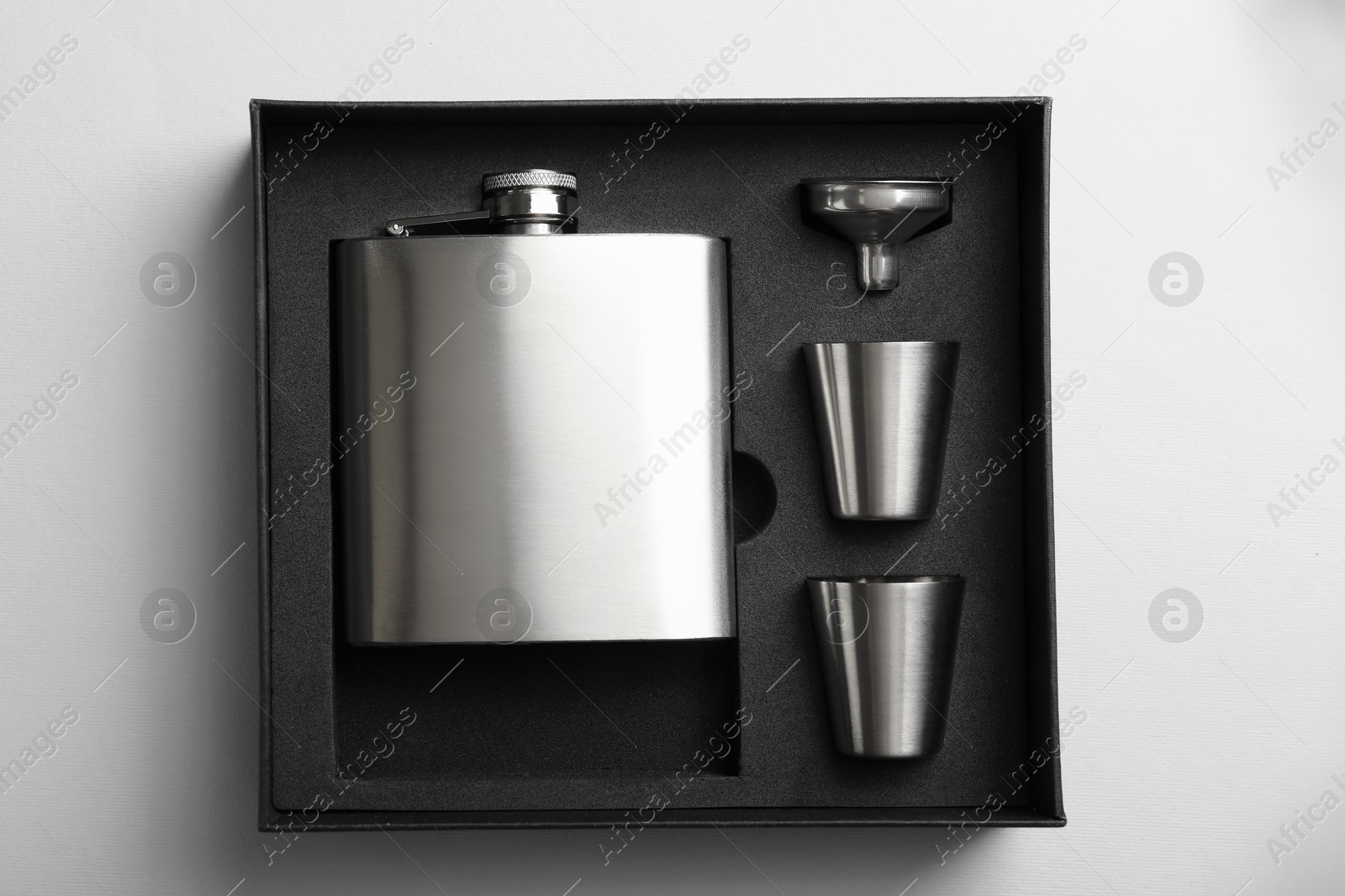 Photo of Hip flask, cups and funnel in package on white background, top view