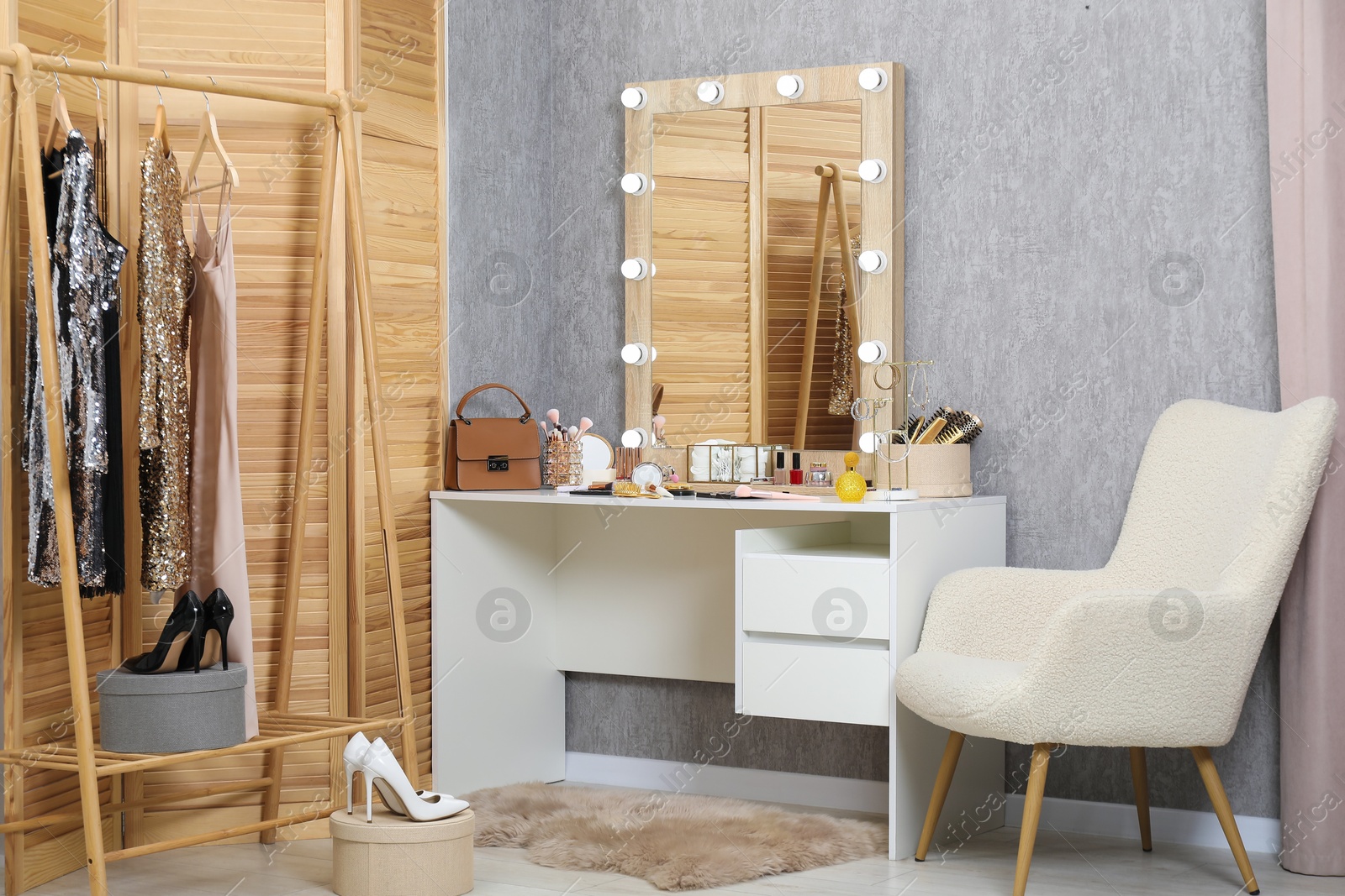 Photo of Makeup room. Mirror, dressing table, different beauty products, clothing rack and armchair indoors