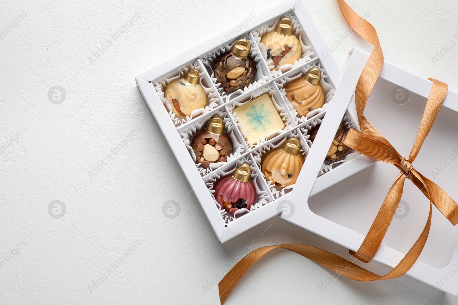 Photo of Box with tasty chocolate candies in shape of baubles on white background, top view. Space for text