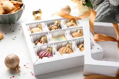 Photo of Box with tasty chocolate candies in shape of baubles and Christmas decor on white background, closeup