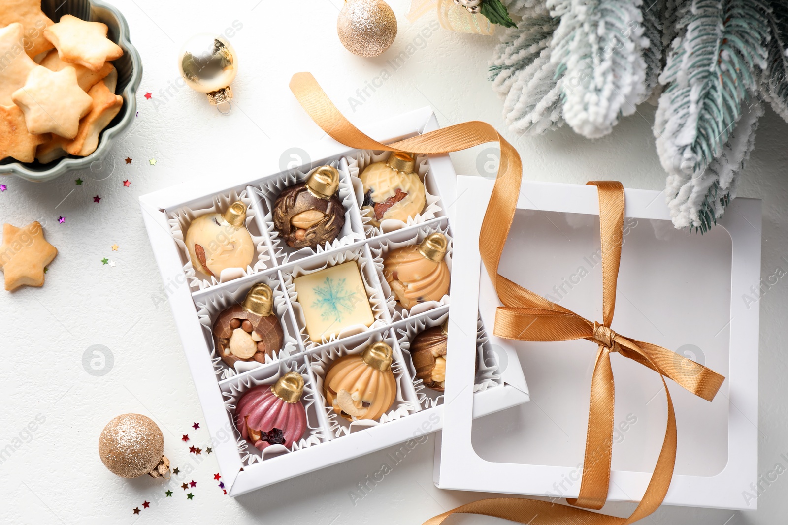 Photo of Box with tasty chocolate candies in shape of baubles and Christmas decor on white background, flat lay