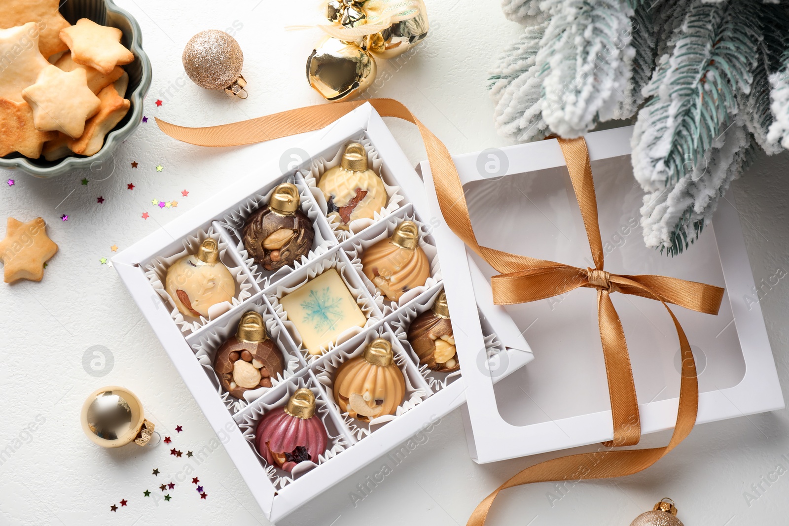 Photo of Box with tasty chocolate candies in shape of baubles and Christmas decor on white background, flat lay