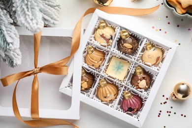 Photo of Box with tasty chocolate candies in shape of baubles and Christmas decor on white background, flat lay