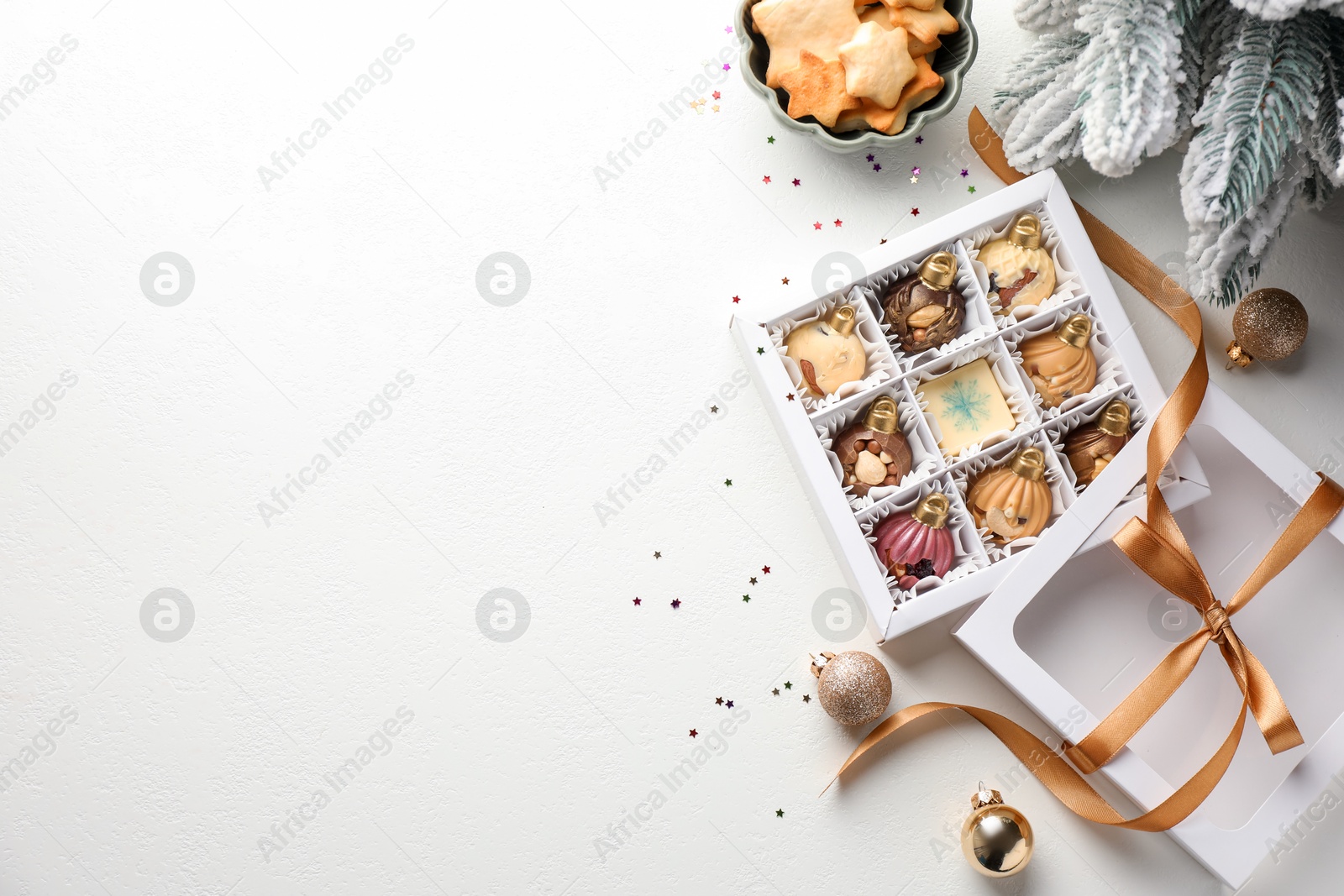 Photo of Box with tasty chocolate candies in shape of baubles and Christmas decor on white background, flat lay. Space for text