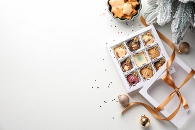 Box with tasty chocolate candies in shape of baubles and Christmas decor on white background, flat lay. Space for text