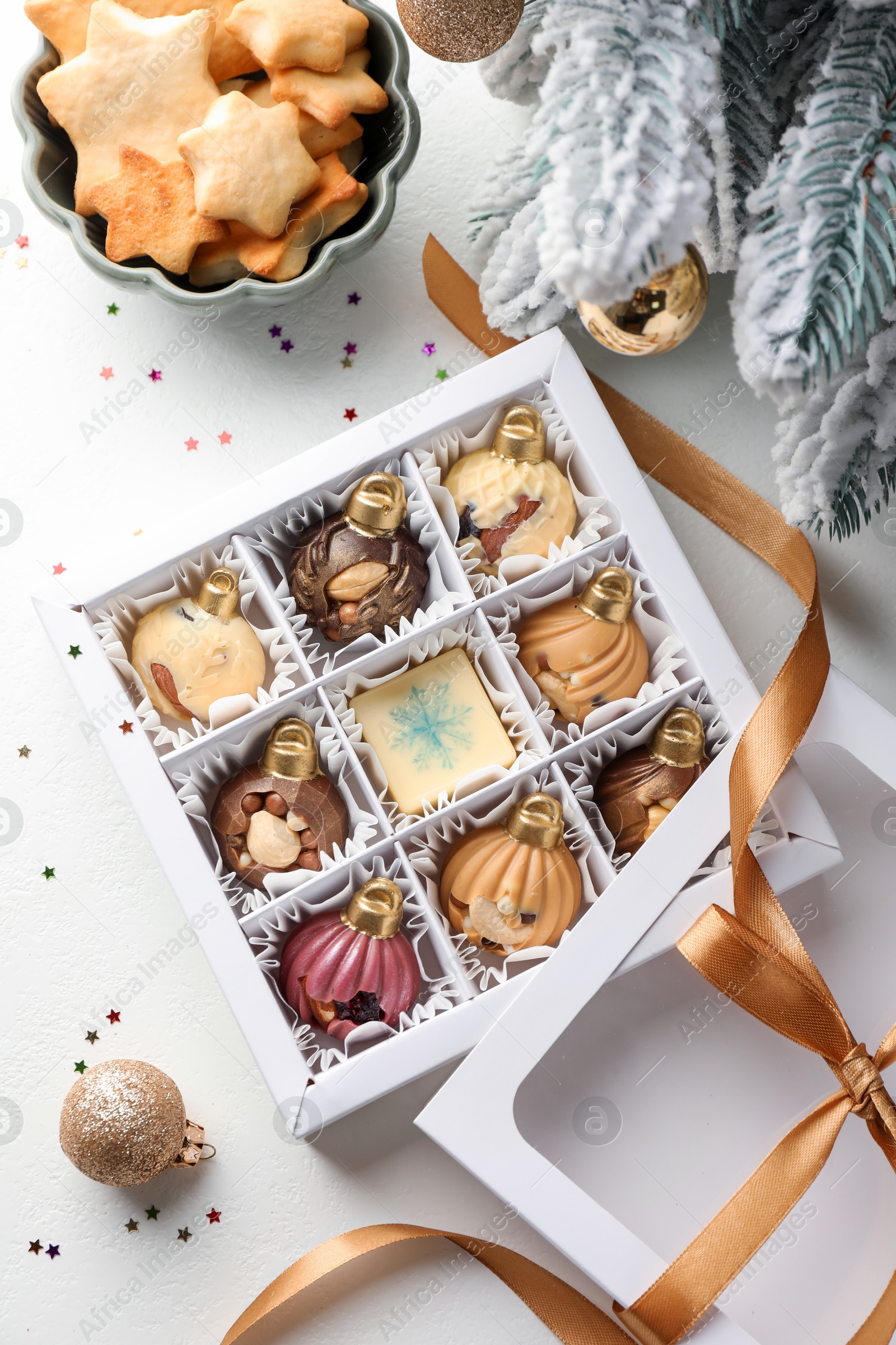 Photo of Box with tasty chocolate candies in shape of baubles and Christmas decor on white background, flat lay