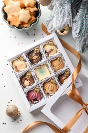 Box with tasty chocolate candies in shape of baubles and Christmas decor on white background, flat lay