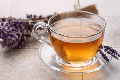 Photo of Aromatic lavender tea in glass cup and dry flowers on white tiled table, closeup