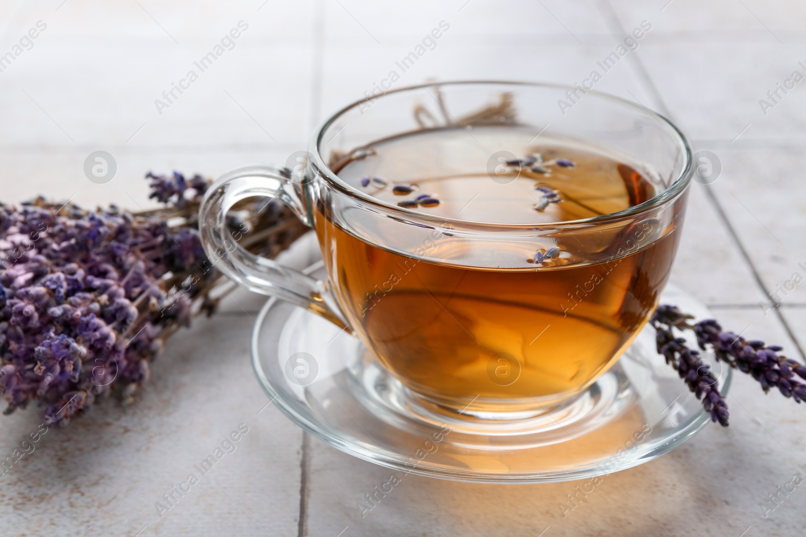 Aromatic lavender tea in glass cup and dry flowers on white tiled table, closeup Photo of Aromatic lavender tea in glass cup and dry flowers on white tiled table, closeup