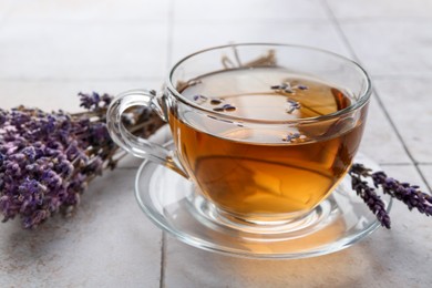 Photo of Aromatic lavender tea in glass cup and dry flowers on white tiled table, closeup