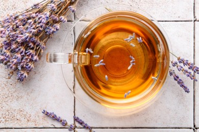 Photo of Aromatic lavender tea in glass cup and dry flowers on white tiled table, flat lay