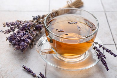 Photo of Aromatic lavender tea in glass cup and dry flowers on white tiled table, closeup