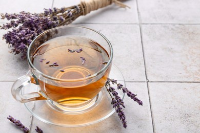 Photo of Aromatic lavender tea in glass cup and dry flowers on white tiled table, closeup. Space for text