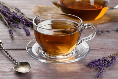 Photo of Aromatic lavender tea in glass cup, spoon and dry flowers on wooden table, closeup