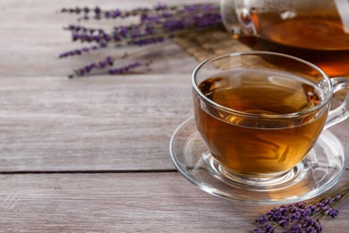 Photo of Aromatic lavender tea in glass cup and dry flowers on wooden table, closeup. Space for text