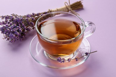 Photo of Aromatic lavender tea in glass cup and dry flowers on pink background, closeup