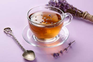 Photo of Aromatic lavender tea in glass cup, spoon and dry flowers on pink background, closeup