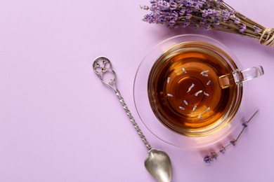 Photo of Aromatic lavender tea in glass cup, spoon and dry flowers on pink background, top view. Space for text