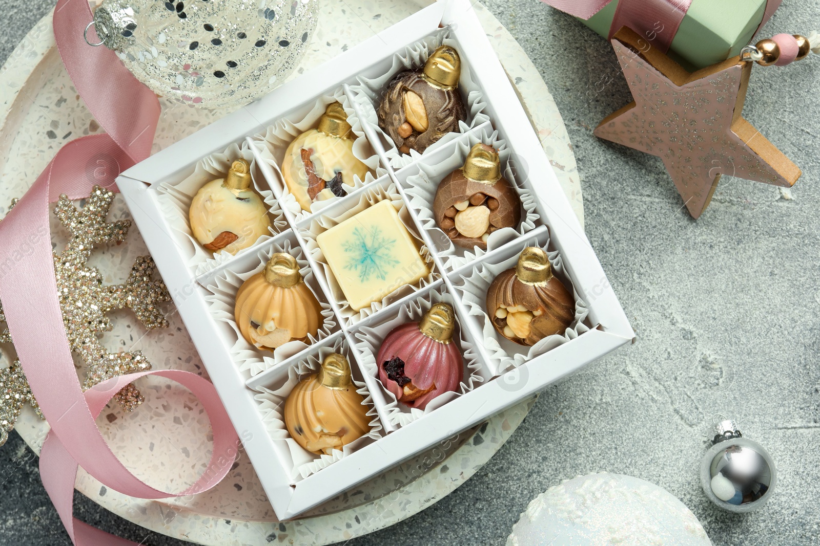 Photo of Box with tasty sweets in shape of baubles and Christmas decor on grey background, flat lay