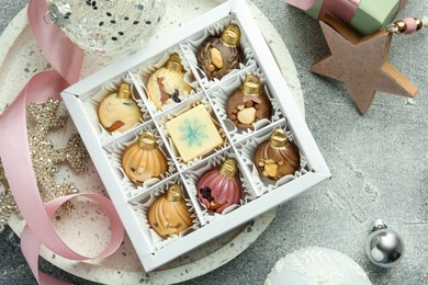 Box with tasty sweets in shape of baubles and Christmas decor on grey background, flat lay