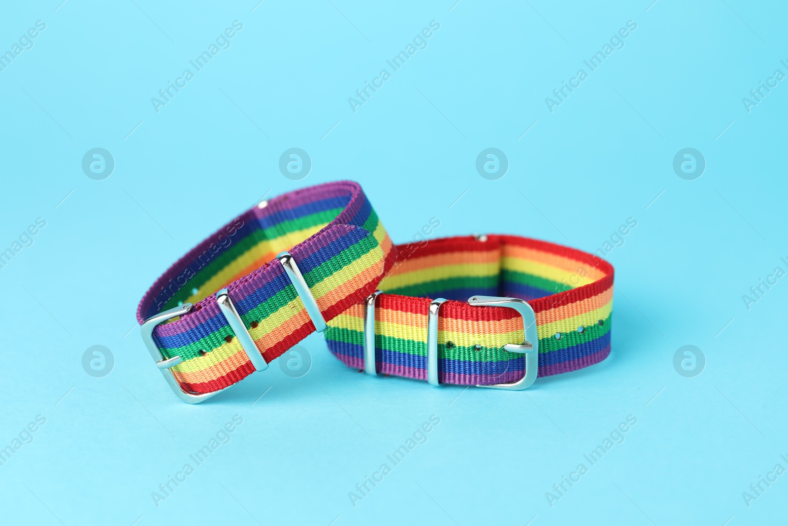 Photo of Two wristbands in LGBT colors on light blue background, closeup