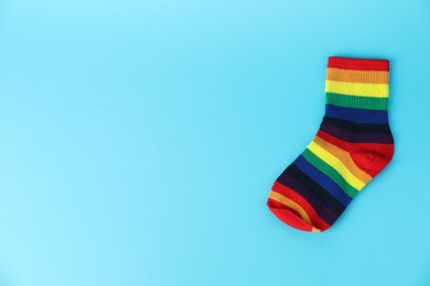 Photo of One sock in LGBT colors on light blue background, top view. Space for text