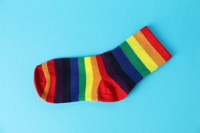 Photo of One sock in LGBT colors on light blue background, top view