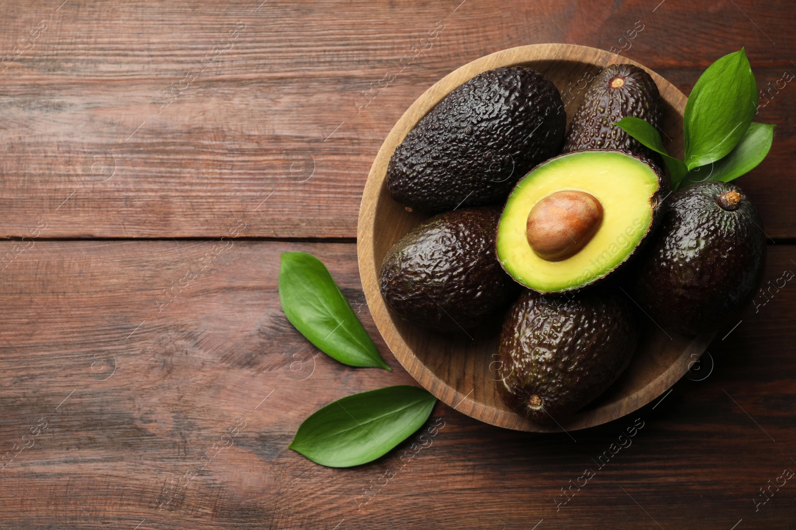 Photo of Fresh ripe avocados and leaves on wooden table, top view. Space for text