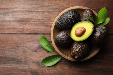 Photo of Fresh ripe avocados and leaves on wooden table, top view. Space for text