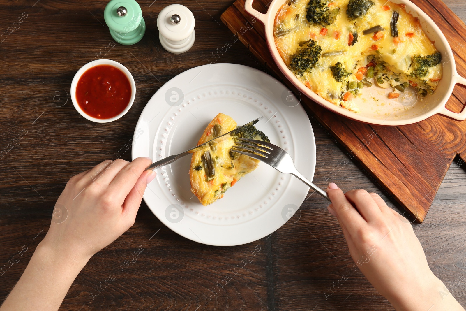 Photo of Woman eating tasty vegetable casserole at wooden table, top view