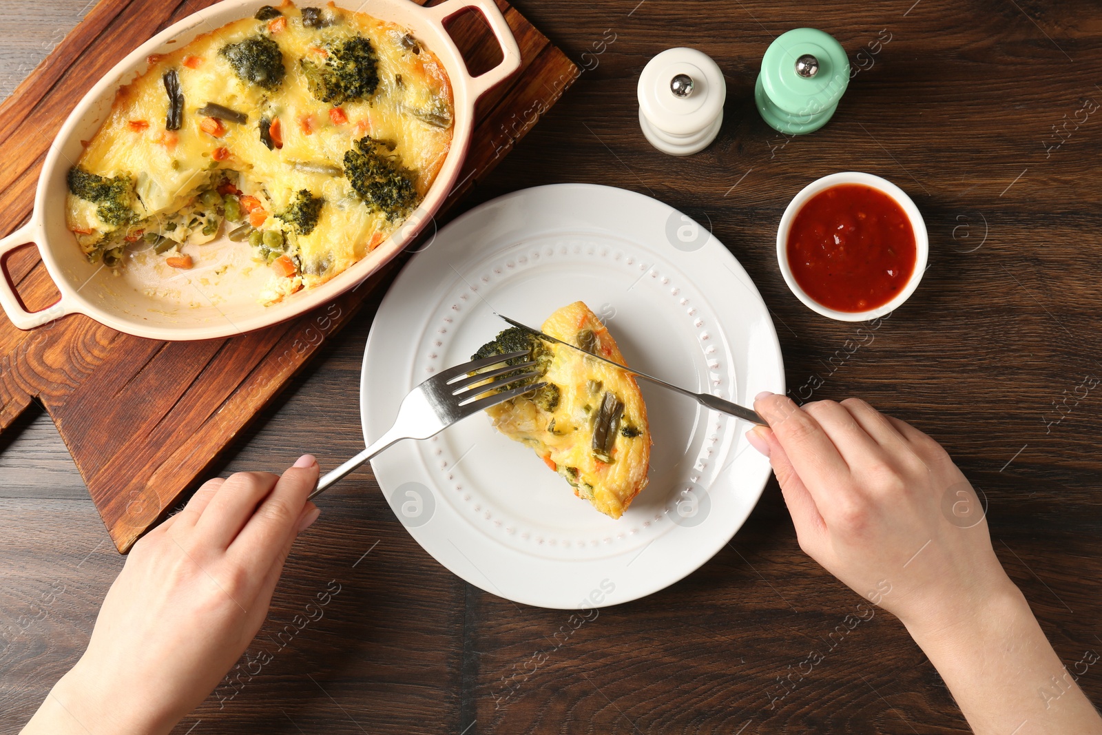 Photo of Woman eating tasty vegetable casserole at wooden table, top view