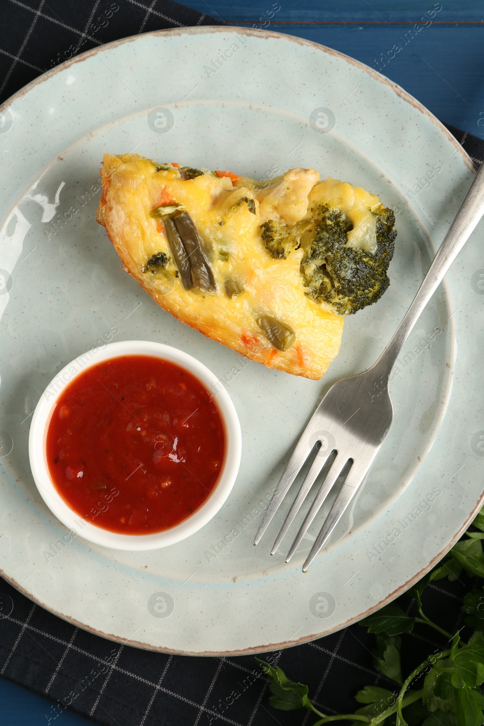 Photo of Piece of tasty vegetable casserole and sauce on blue wooden table, top view