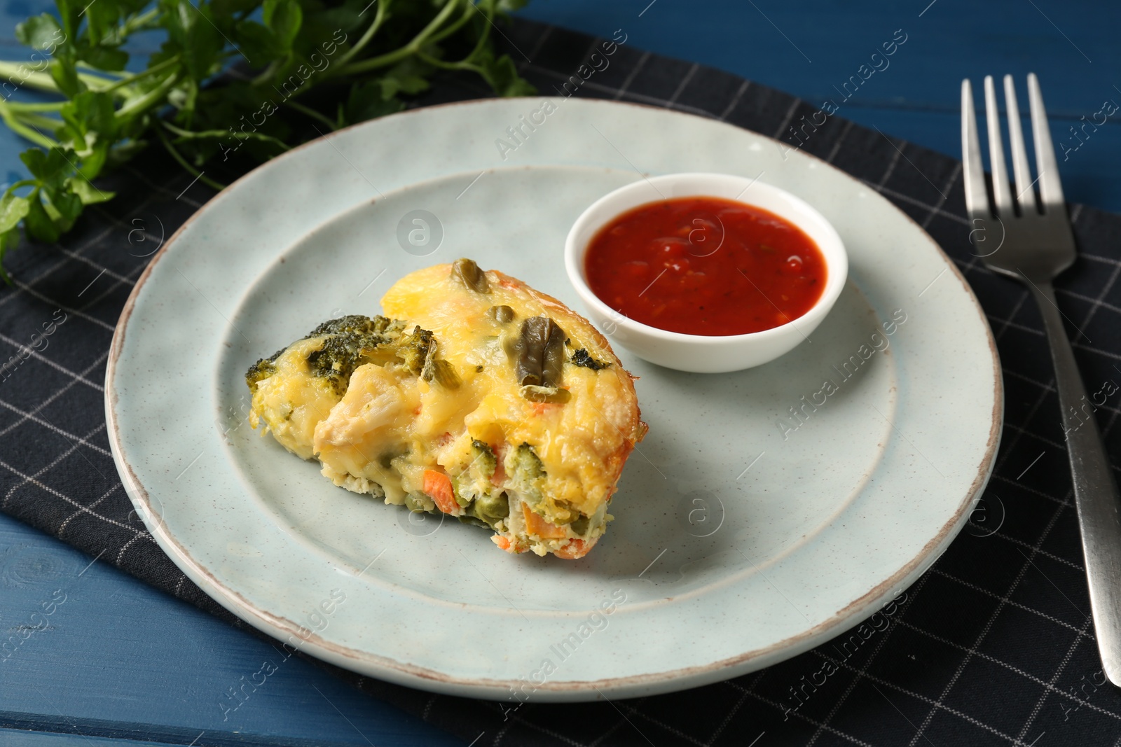 Photo of Piece of tasty vegetable casserole and sauce on blue wooden table, closeup