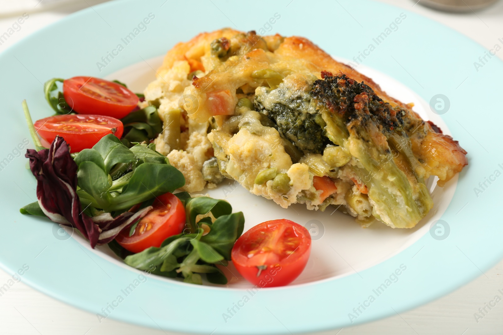 Photo of Tasty vegetable casserole and salad on white wooden table, closeup