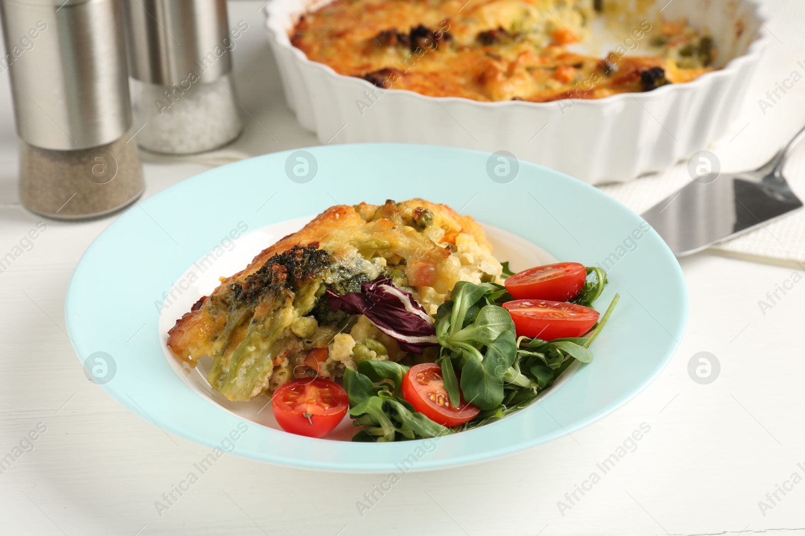 Photo of Tasty vegetable casserole and salad on white wooden table, closeup