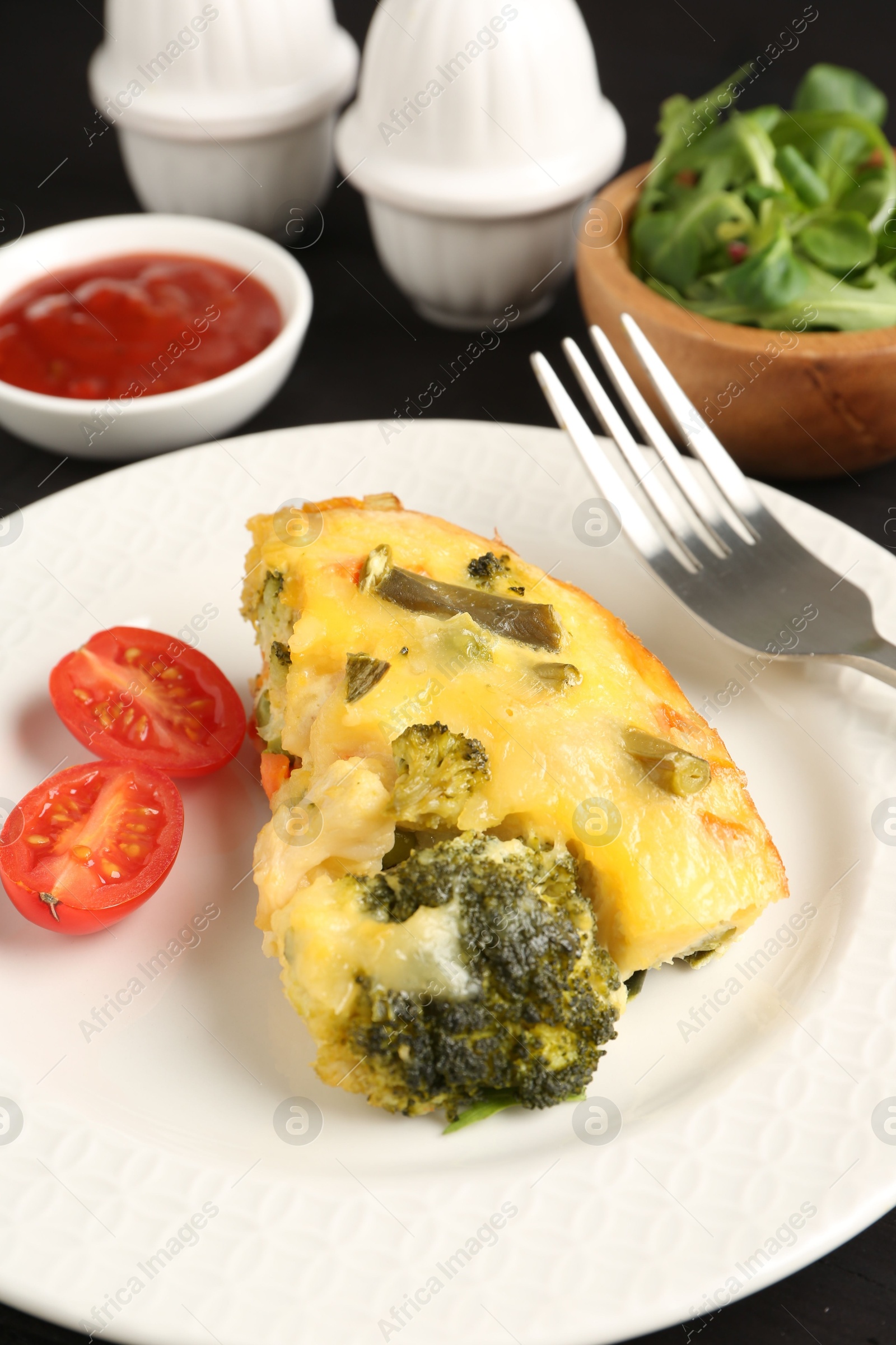 Photo of Tasty vegetable casserole and tomato on black table, closeup