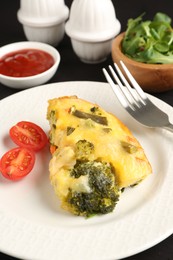 Photo of Tasty vegetable casserole and tomato on black table, closeup